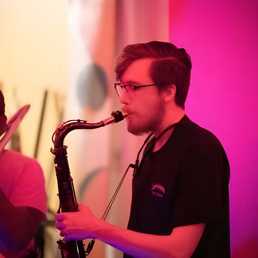 Musician wearing glasses plays saxophone under pink and purple stage lighting